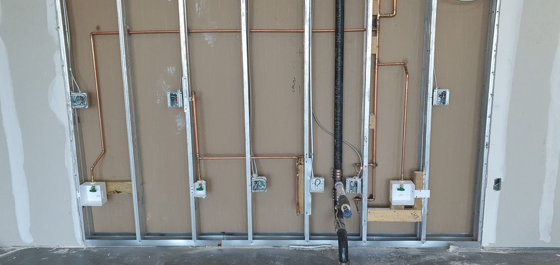 Copper water supply lines and black gas piping roughed into a steel-framed wall