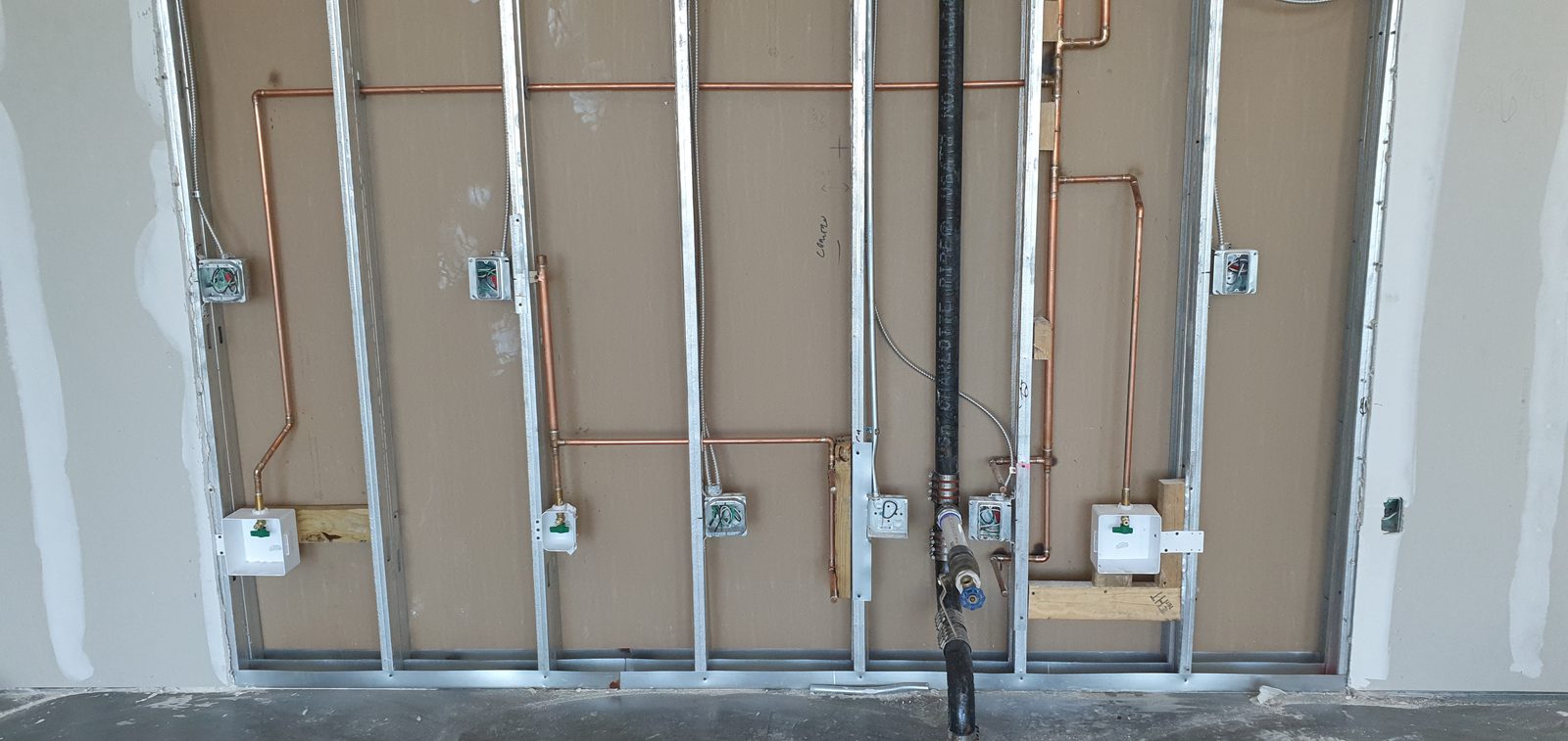 Copper water supply lines and black gas piping roughed into a steel-framed wall with washer and hose-bib boxes