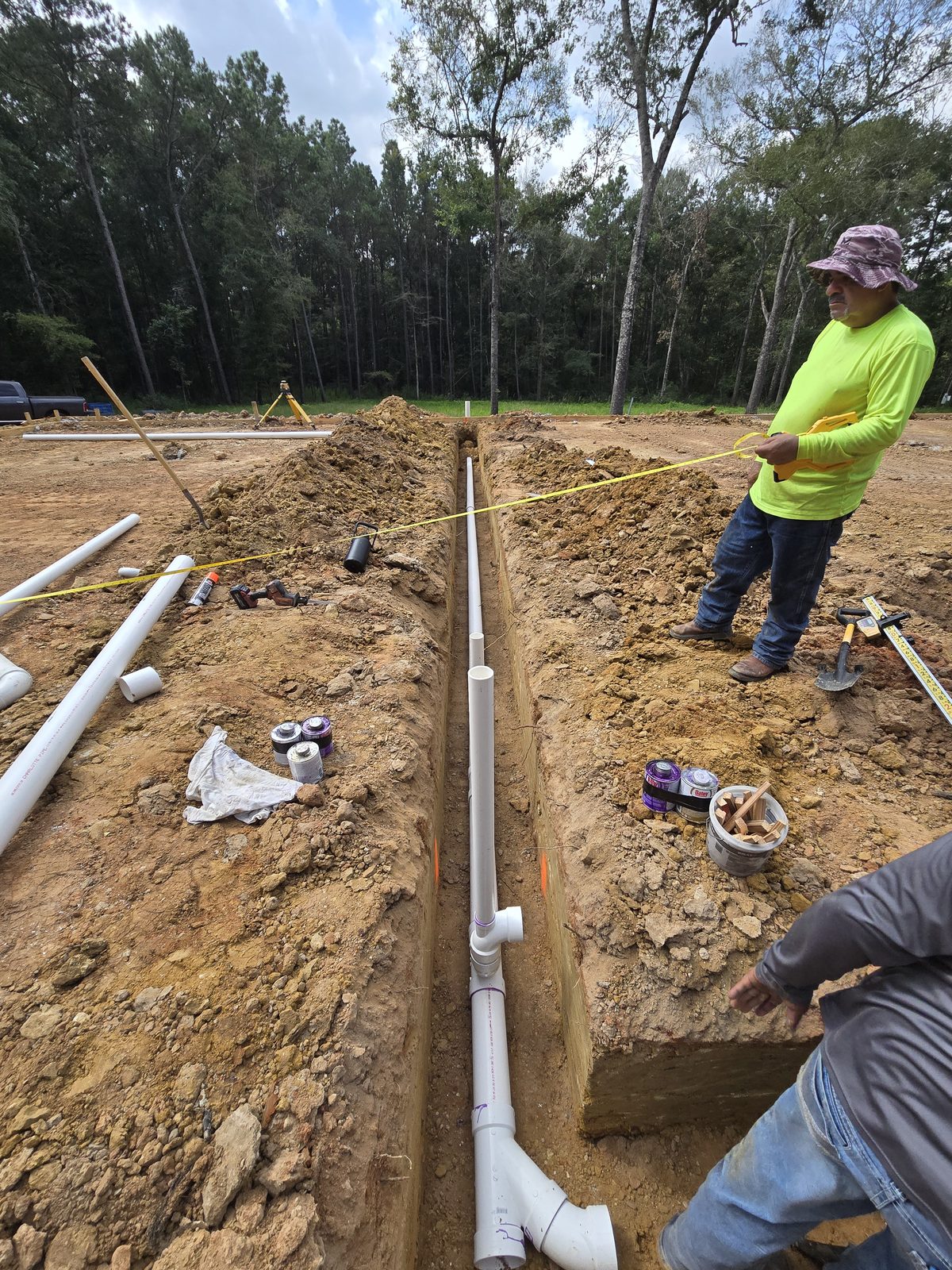 Underground sanitary sewer rough-in with PVC drain lines laid to grade in a trench, laser level in background